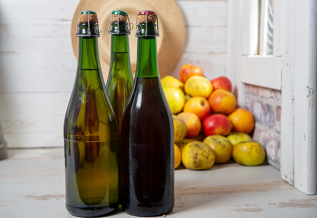 Bouteilles de cidre entourées de pommes fraîches en Normandie.